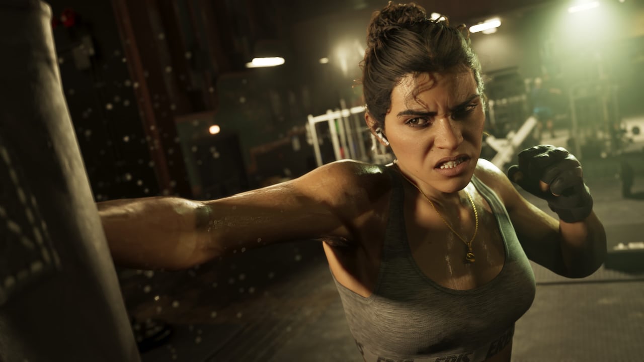 Lucia Caminos punches a heavy bag in a dim gym, sweating in a grey tank top with a gold chain and fingerless gloves, in official GTA VI artwork